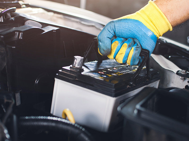 Person mit Handschuh entnimmt eine alte Autobatterie aus dem Fahrzeug zum Wechseln.