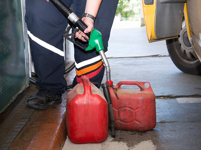 Person betankt zwei alte Benzinkanister an einer Tankstelle.