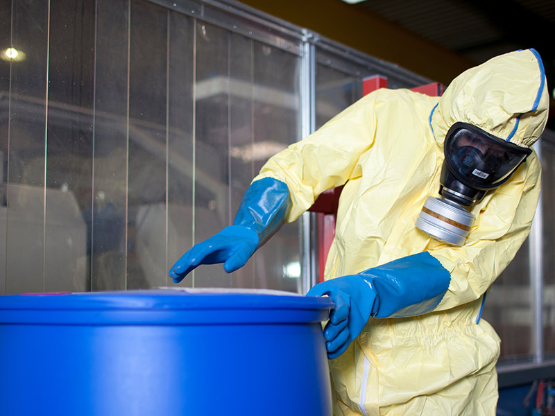 Person in Schutzkleidung schließt sorgfältig einen Behälter mit Chemikalien.