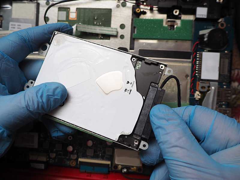 Person mit Handschuhen entnimmt eine Festplatte aus einem Computer.