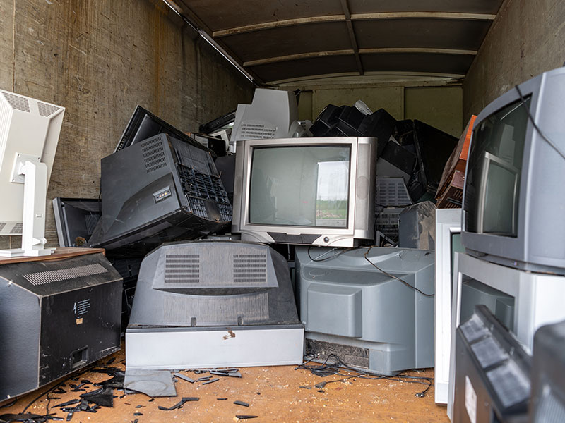 Alte Fernseher liegen in einem Container bereit zur Entsorgung.