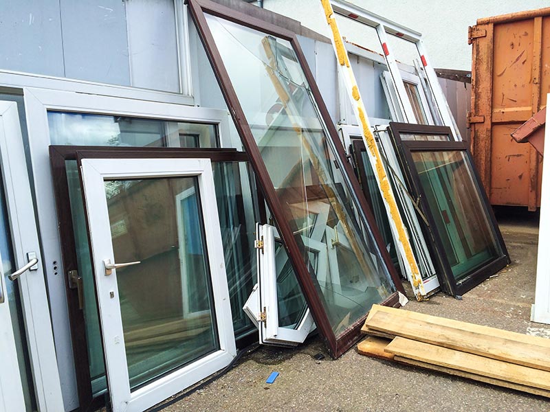 Alte Fenster verschiedener Größe stehen vor einer Gebäudewand.