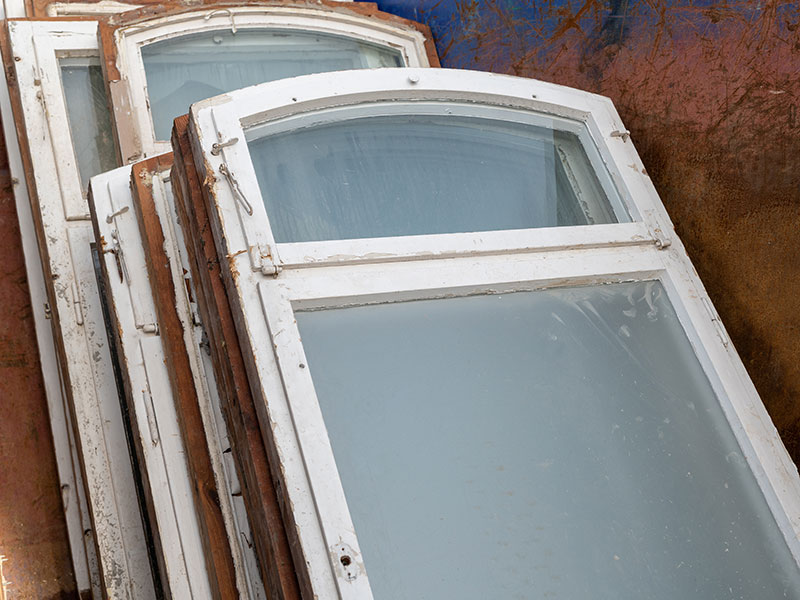 Mehrere alte Holzfenster liegen in einem Container.