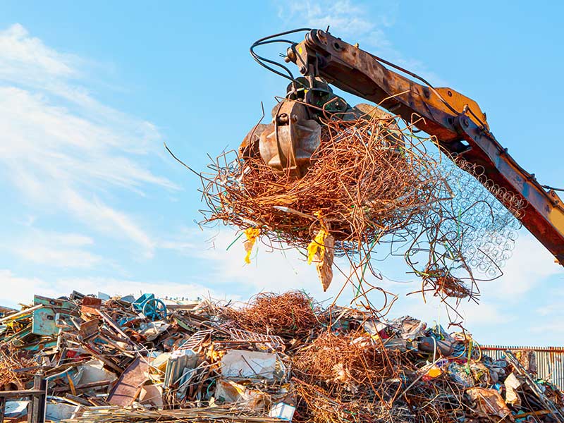 Kranarm auf einer Recyclinganlage greift Altmetall und Schrott auf.